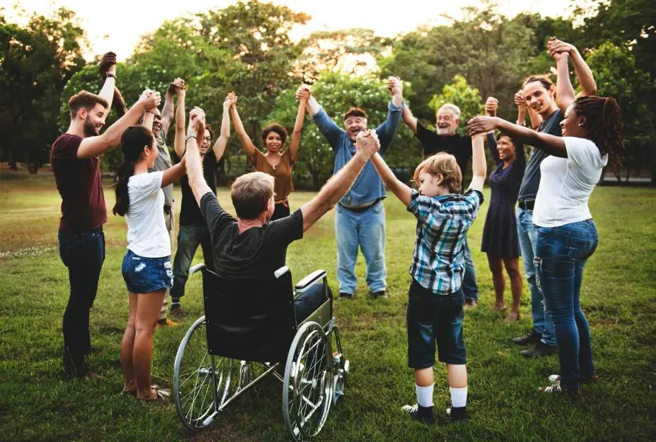 Group of people, including a participant using a wheelchair, joining hands in a circle outdoors